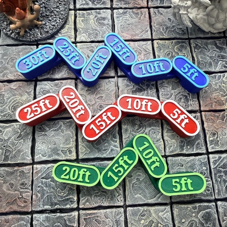 Op de afbeelding: Een verzameling gekleurde, gebogen spelmarkeringen in blauw, rood en groen, elk gemarkeerd met afstanden in voet: 5ft, 10ft, 15ft, 20ft, 25ft en 30ft. De markeringen liggen op een grijze, getextureerde ondergrond.