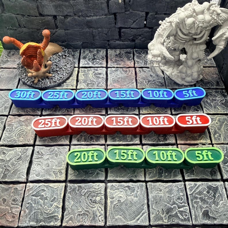 Op de afbeelding: Drie rijen kleurrijke afstandsaanduidingen voor tabletop gaming. De bovenste rij is blauw, de middelste rij is rood en de onderste rij is groen. Elke marker geeft afstanden in voet weer, vari&euml;rend van 5ft tot 30ft.