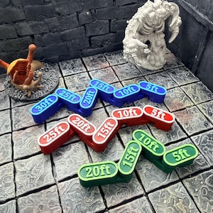 Op de afbeelding: Een verzameling kleurrijke plastic spelafstandmarkeringen. De markeringen zijn blauw, rood en groen, met witte tekst die afstanden in voet aangeeft: 5ft, 10ft, 15ft, 20ft, 25ft en 30ft. Voor tabletop rollenspellen.
