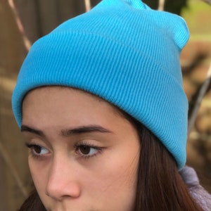 May include: A person wearing a bright blue beanie. The beanie is made of a soft, knitted fabric.