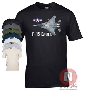 Puede incluir: Camiseta negra con una silueta blanca de un avión de combate F-15 Eagle y el texto "F-15 Eagle". El avión tiene una insignia de estrella y barra de la Fuerza Aérea de los Estados Unidos en la cola.