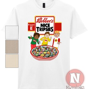 Puede incluir: Camiseta blanca con una ilustración de dibujos animados de tres niños comiendo un tazón de cereal llamado "Klubber's Nice Tripsies" con el texto "Fortified with E" en la caja.