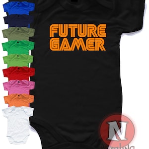Può includere: Body nero per neonato con testo arancione che recita "FUTURE GAMER" in un font in stile retrò da videogioco. Il body è mostrato con una varietà di opzioni di colore.