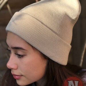 May include: A beige knitted beanie hat with a ribbed texture. The hat is folded down at the brim.