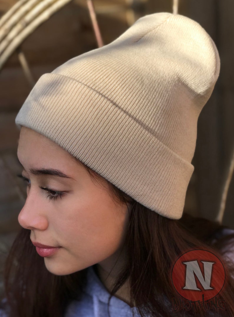 May include: A beige knitted beanie hat with a ribbed texture. The hat is folded down at the brim.