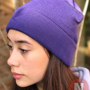 May include: A purple beanie hat made of knitted fabric. The hat is folded down at the brim and has a slouchy fit.