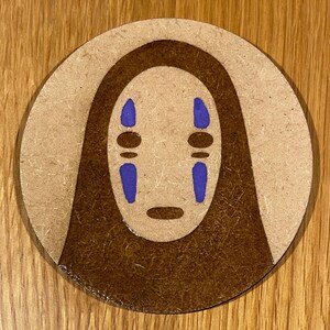 May include: A round, brown wooden coaster featuring a brown and purple No Face character from the film Spirited Away.