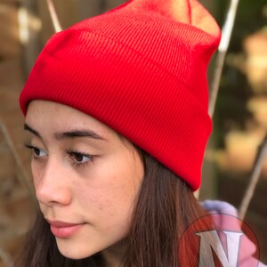 May include: A red knit beanie hat. The hat is folded down at the top and has a ribbed texture.