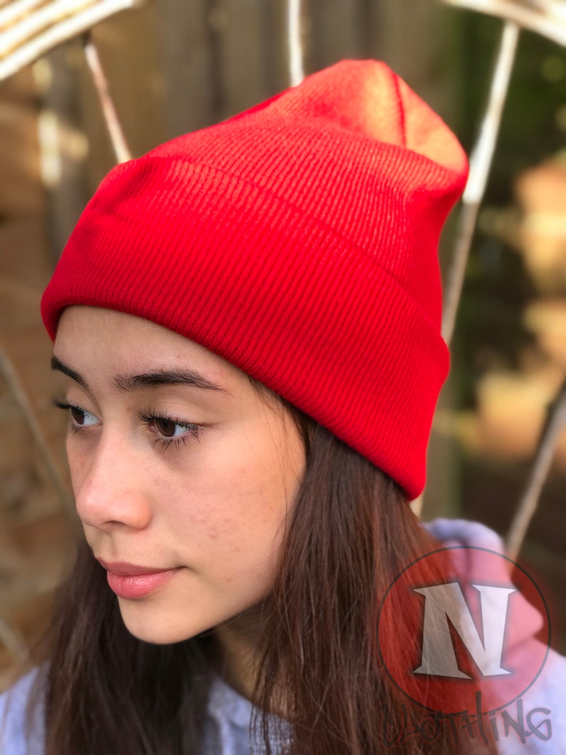 May include: A red knit beanie hat. The hat is folded down at the top and has a ribbed texture.