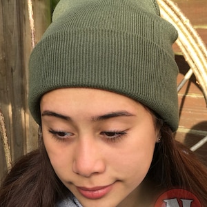 May include: A green knitted beanie hat. The hat is made of a soft, comfortable material and has a simple, classic design.