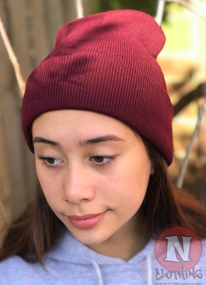 May include: A close-up of a person wearing a maroon beanie. The beanie is made of a soft, knitted fabric. The person is looking down and has a neutral expression.