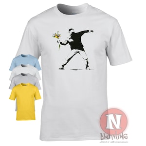 Peut inclure: T-shirt blanc avec un imprimé graphique noir et blanc d'une personne lançant un bouquet de fleurs. Le graphique est une œuvre d'art de rue célèbre de Banksy.