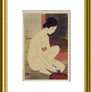 May include: A framed Japanese woodblock print depicting a figure with dark hair styled in an updo, crouching while washing feet in a dark red basin. The scene features a textured gray floor, a yellow bamboo-patterned screen, and a dark cloth.