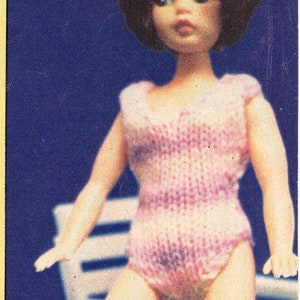 May include: A pink and white striped crocheted swimsuit with matching leg warmers. The doll is sitting on a white chair.