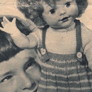 May include: A young girl holds a doll with curly hair wearing a striped knitted dress. The doll has a sweet expression and is looking at the camera.