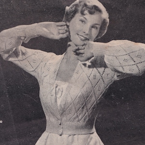 May include: A close-up of a woman wearing a white cardigan with a diamond pattern. The cardigan has a button closure and is knitted with a delicate stitch.