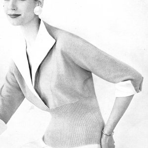 May include: A woman wearing a light gray sweater with a white collar and a white undershirt. The sweater has a fitted waist and three-quarter sleeves. She is wearing a silver bracelet on her wrist.