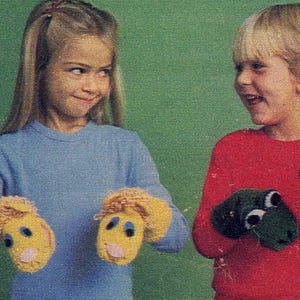 Op de afbeelding: Twee kinderen dragen gebreide vingerpoppen. Het meisje draagt een blauwe trui en gele leeuwenvingerpoppen. De jongen draagt een rode trui en groene kikkervingerpoppen.