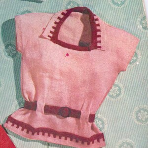 Op de afbeelding: Een vintage roze gebreide top met een contrasterende donkerrode kraag, riem en zoom. De top heeft een kraag en een riemdetail in de taille. De top met korte mouwen komt waarschijnlijk uit een retro mode-tijdperk.