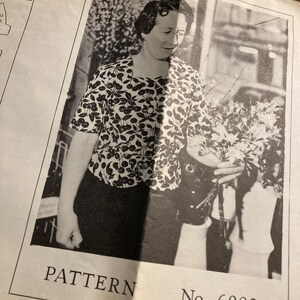 May include: Black and white photograph of a woman wearing a black and white patterned blouse and holding a bouquet of flowers. The photo is from a vintage sewing pattern and includes the text "PATTERN No. 6082".