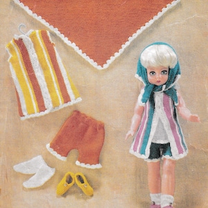 May include: A set of knitted doll clothes, including a striped vest, orange shorts, white socks, yellow shoes, a teal vest with pink stripes, and a teal and white scarf. The doll clothes are laid out on a brown background.