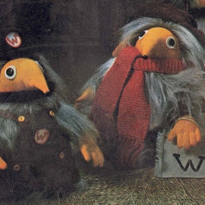 May include: Two whimsical, plush figures with orange beaks and large eyes. One wears a dark uniform with a "W" badge, the other a red scarf. Both have gray fur and small orange hands. One holds a bag with a "W".