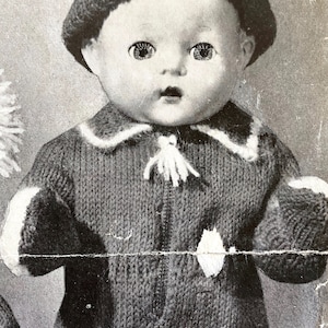 Può includere: Una bambola di lana che indossa un completo di lana grigio con un cappello bianco con pon pon. La bambola ha un bordo bianco di lana intorno al collo e ai polsi.