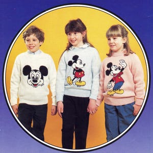 Könnte beinhalten: Drei Kinder tragen gestrickte Pullover mit einem Mickey-Mouse-Motiv. Die Pullover sind in Weiß, Hellblau und Rosa. Die Kinder halten sich an den Händen und lächeln.