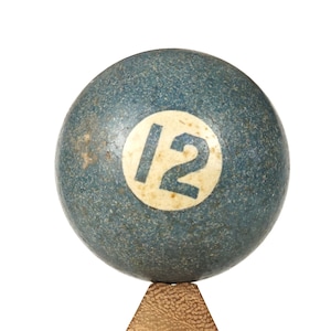 Könnte beinhalten: Eine blaue Billardkugel mit der Nummer 12, die in weiß darauf gedruckt ist. Die Kugel liegt auf einem Holzständer.