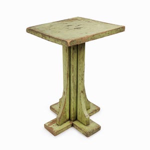 May include: A square-topped side table with a distressed light green painted finish. The table features a central pedestal base supported by a cross-shaped foot, showing visible wood grain and worn edges throughout the entire structure.