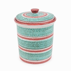 Pode incluir: Um recipiente de cerâmica com tampa. O recipiente é cilíndrico com um acabamento turquesa salpicado e listras horizontais vermelhas e brancas. A tampa tem um design correspondente e um pequeno botão vermelho. O design geral é vintage.