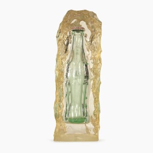 Könnte beinhalten: Eine Vintage-Glasflasche von Coca-Cola, eingebettet in klarem Harz, das einem Eisblock ähnelt.