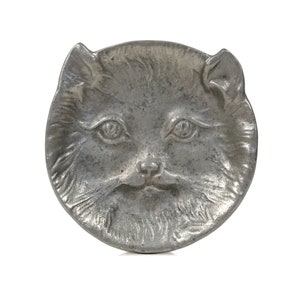 Puede incluir: Un plato de metal plateado con forma de cara de gato. El plato tiene un dise&ntilde;o detallado de la piel y las caracter&iacute;sticas de un gato.