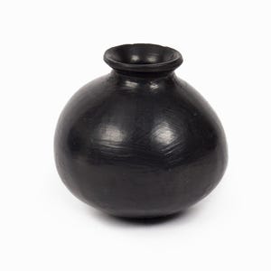 Peut inclure: Un petit vase noir arrondi avec une surface lisse et légèrement réfléchissante. Le récipient présente un corps large et bulbeux qui se rétrécit vers le haut en un col court et étroit avec une ouverture à bord circulaire évasé au sommet.