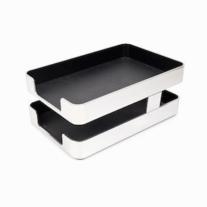 May include: Two-tier silver-colored desk organizer with black interior. The trays are rectangular with a cutout on one side for easy access. The organizer is designed for office or home use, providing a stylish way to store documents and papers.