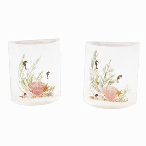 May include: Two clear glass candle holders with a seashell, starfish, and seahorse design. The holders are filled with sand and small seashells.