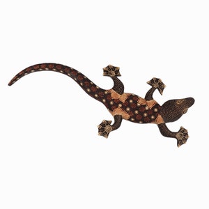 May include: A wooden gecko wall decor with a black and brown batik pattern. The gecko has a long tail and is in a running pose.