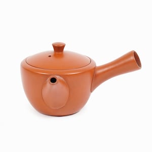 Könnte beinhalten: Eine Terrakotta-Teekanne mit rundem Korpus und einem langen, gebogenen Ausguss. Die Teekanne hat einen Deckel mit einem kleinen Knopf oben.