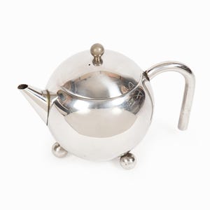 Może przedstawiać: Polerowany, kulisty czajnik ze stali nierdzewnej z zakrzywionym uchwytem i małym dziobkiem. Czajnik ma pasującą pokrywkę z małym pokrętłem i spoczywa na trzech zaokrąglonych nóżkach. Powierzchnia odbijająca światło.