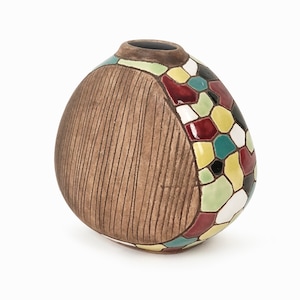 May include: A brown ceramic vase with a textured surface and a colourful geometric design on one side. The design features red, yellow, green, blue, and white colours.