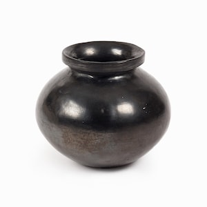 Peut inclure: Un pot en céramique noir, de forme arrondie avec une ouverture étroite. La surface est lisse et réfléchissante, suggérant une fabrication artisanale. La couleur sombre et le design simple évoquent un style rustique ou traditionnel.
