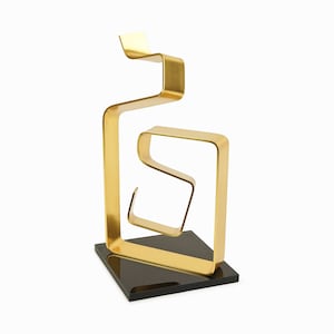 May include: A gold metal sculpture with a geometric design. The sculpture is made of multiple interlocking loops and stands on a black base.