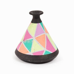 Puede incluir: Un pequeño jarrón decorativo con un patrón geométrico. El jarrón tiene una base y una parte superior negras, con un cuerpo en forma de cono. El cuerpo está decorado con un colorido patrón geométrico en tonos rosa, naranja, verde y amarillo.