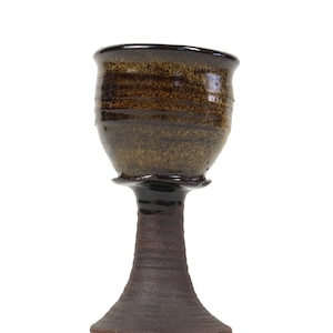 May include: A brown and black ceramic goblet with a wide base and a flared lip. The goblet has a speckled glaze and a dark brown interior.