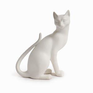 Może przedstawiać: Biała ceramiczna figurka kota w pozycji siedzącej z zakręconym ogonem. Kot ma elegancki, minimalistyczny design z gładkim, matowym wykończeniem. Figurka jest przedmiotem dekoracyjnym.