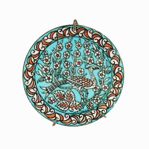 May include: Circular turquoise decorative plate with a bird and floral design. The bird has a white body with brown and orange details. The plate has an orange and white border and a metal hanging loop.