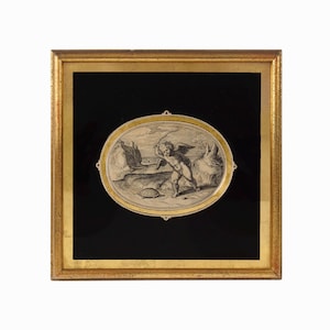 May include: A framed black and white print featuring a winged cherub figure holding a whip while standing near a turtle on a sandy landscape. The artwork is set within an oval mat and enclosed in a square, textured gold-toned wooden frame.