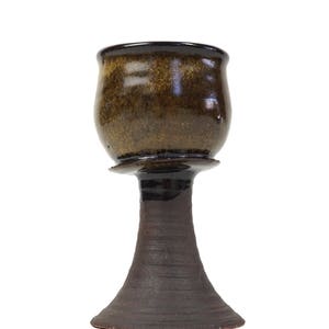Puede incluir: Un cáliz de cerámica marrón y negro con una base ancha. El cáliz tiene un acabado brillante y una superficie texturizada.