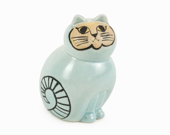 Może przedstawiać: Ceramiczna figurka kota w jasnoniebieskim kolorze z czarnymi i żółtymi detalami malowanymi. Kot ma zwinięty ogon i kapryśny wyraz twarzy.