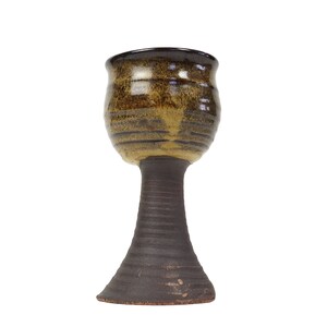 May include: A brown and yellow ceramic goblet with a wide base. The goblet has a dark brown rim and a textured surface.